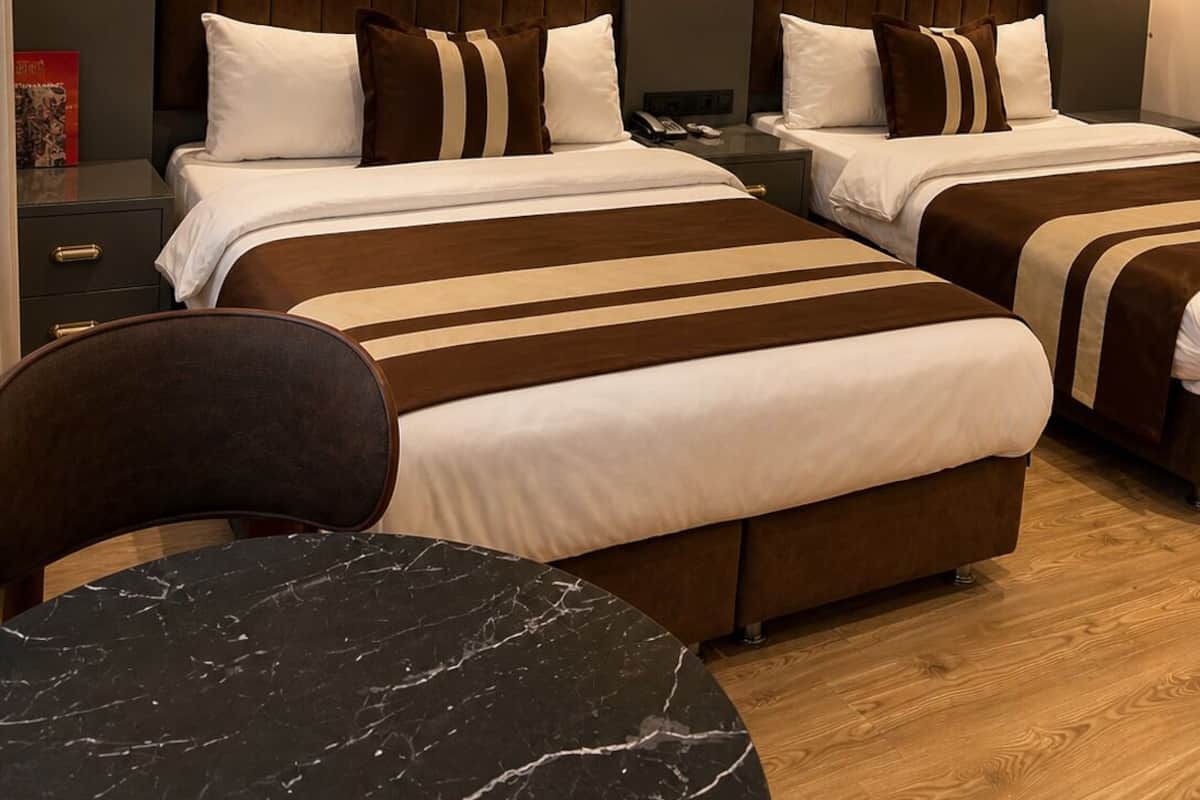 A hotel room with two beds, a marble table, and a brick-patterned wall.