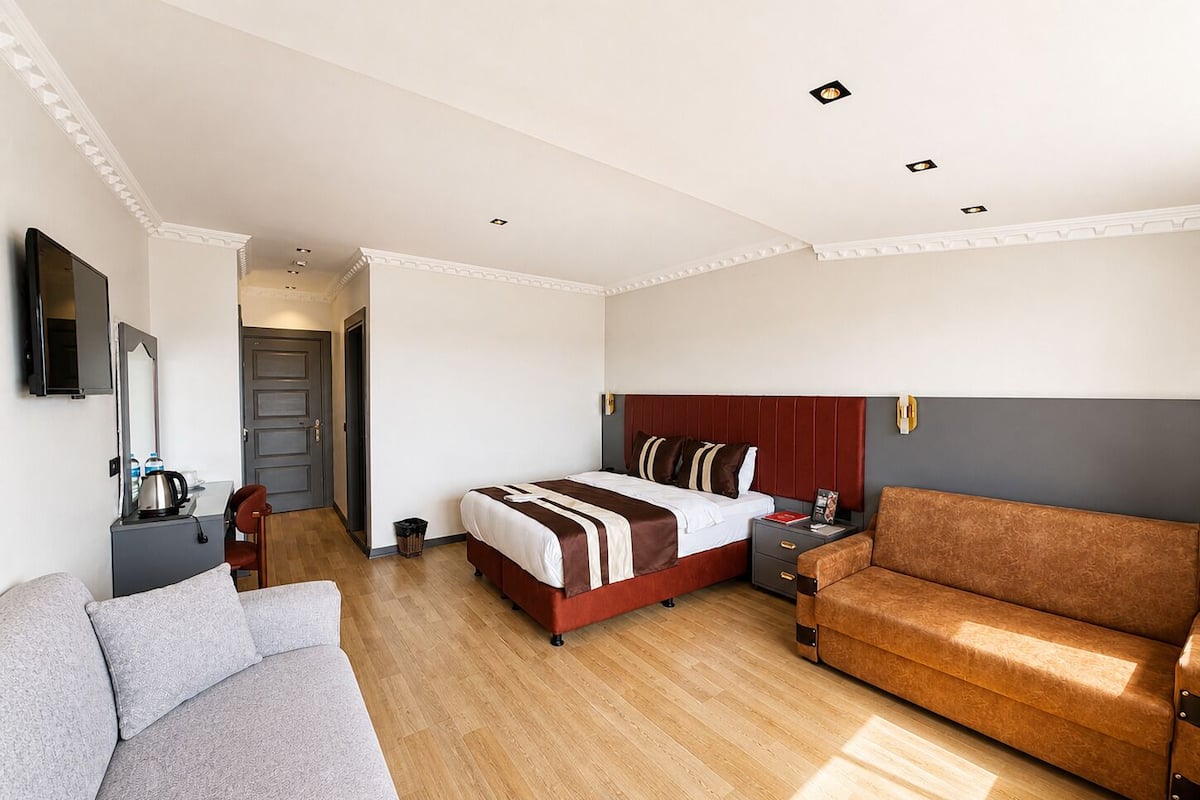 A hotel room with a bed, a sofa, a desk with a mirror, and a television.