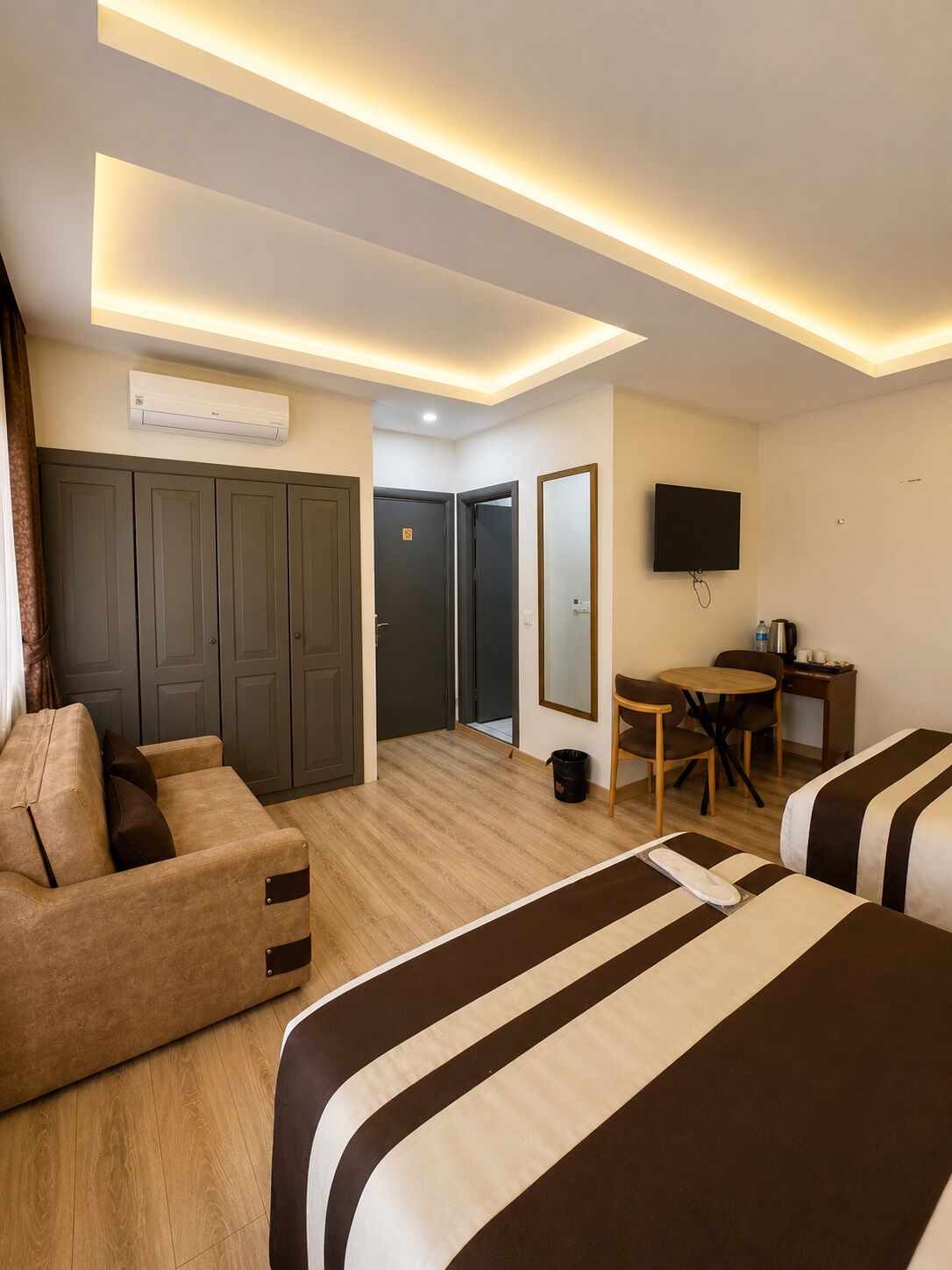 A hotel room with a sofa, a bed, a desk, a television, and a wardrobe.