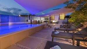 Ett poolområde med solstolar och en möblerad sittplats under tak.