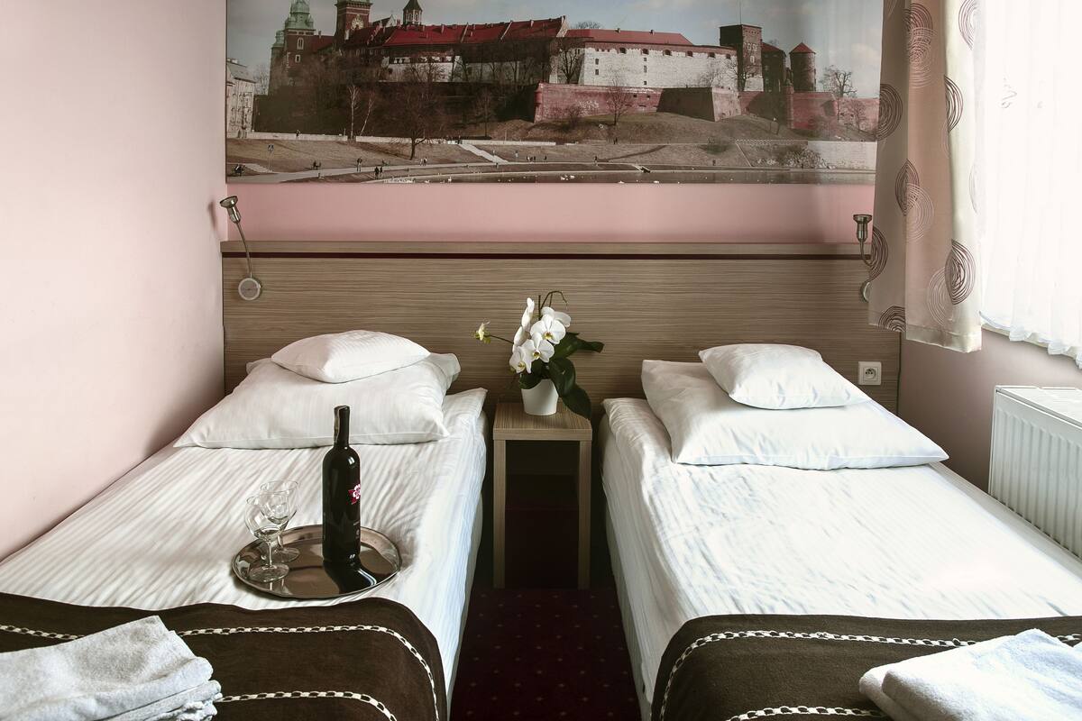 Habitación de hotel con dos camas individuales, una mesita de noche con una botella y un vaso, y un mural en la pared con un castillo.