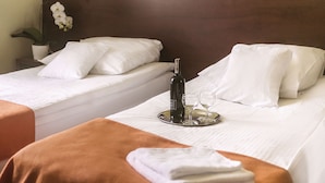 Habitación de hotel con dos camas, una bandeja con una botella y vasos, y una planta en maceta.