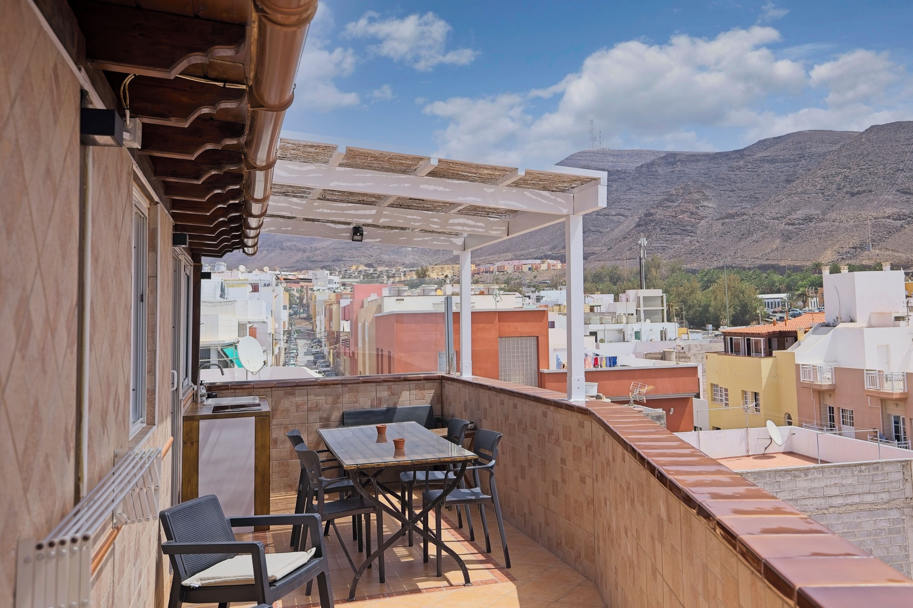 Un balcon avec une table et des chaises, d’où l’on peut admirer une vue sur la ville, avec ses bâtiments et ses montagnes.