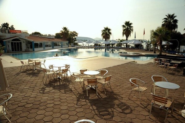 A pool area with hexagonal paving, outdoor seating, and palm trees. - Club Muskebi (Bodrum)