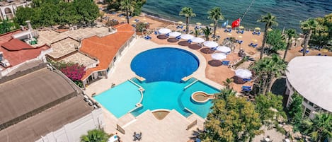 Vista aérea de un complejo turístico con piscina central, tumbonas y zona de playa.