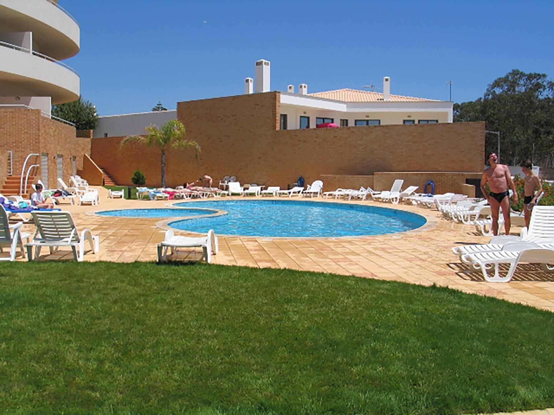 Un espace piscine avec des chaises longues et, en arrière-plan, un bâtiment en briques.