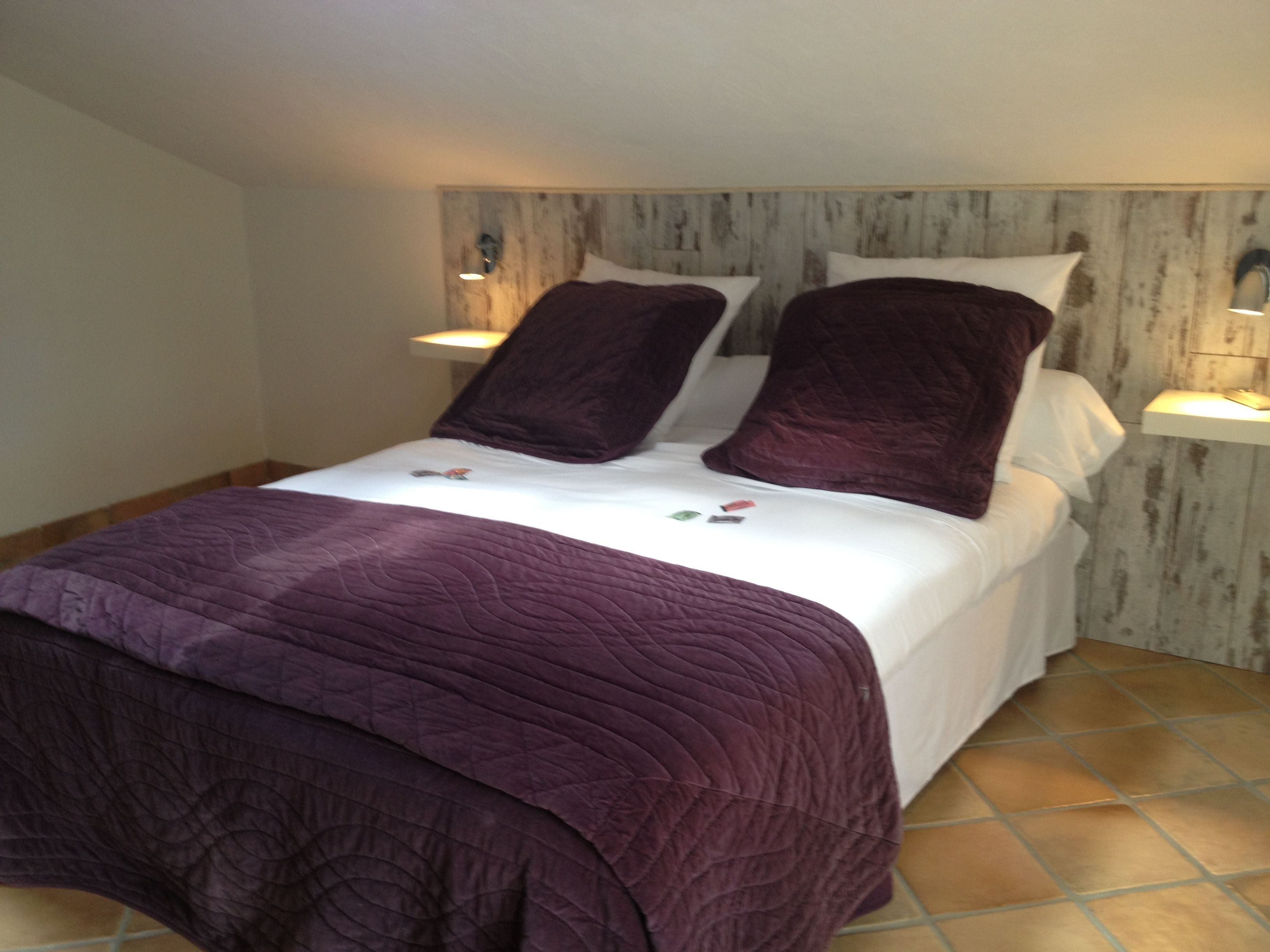 Ein Bett mit einer violetten Bettdecke, weißen Kissen und einem Holzkopfstück.