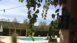A backyard with a swimming pool, a pergola, a red bucket, and a stone planter. - La Vignarelle (Callas)