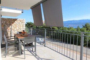 Een balkon met een tafel en stoelen, een stenen muur en uitzicht op een waterpartij en bergen.