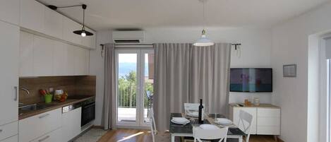 A modern kitchen with a dining area, a TV, and a balcony.