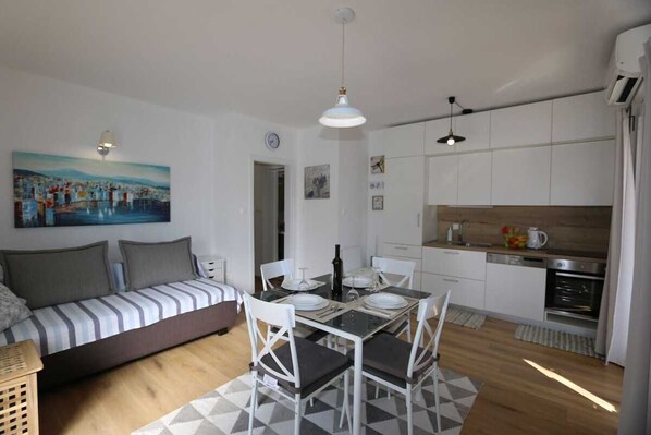 Een functionele woonruimte met een bank, eettafel, stoelen en een keukenhoek.