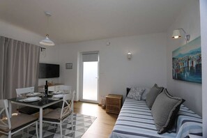 Quarto com mesa de jantar, cadeiras, sofá, televisão, quadro e porta que dá para o exterior.