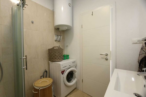 Un baño pequeño con ducha, lavadora, inodoro y lavamanos.