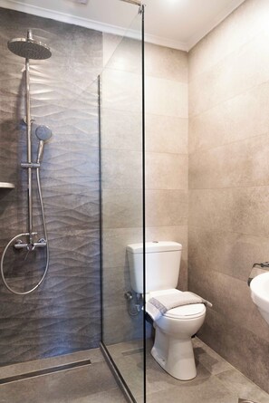 A modern bathroom with a glass-enclosed shower, a toilet, and a sink. - Pink House Socrates (Corfu)