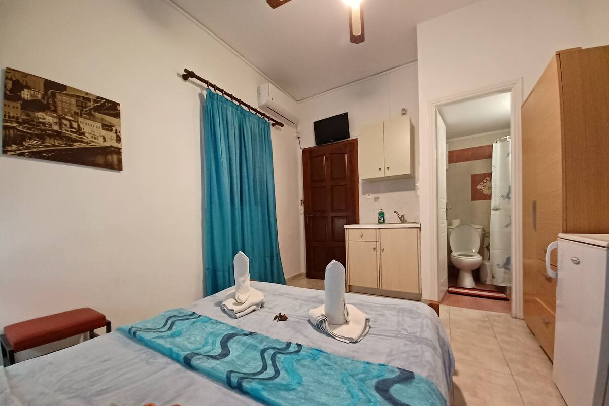Un dormitori amb un llit, una banca, un bany visible a través d'una porta oberta i un aire condicionat fixat a la paret.