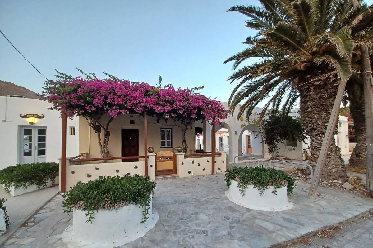 Un edifici tradicional amb un pati empedrat de pedra, una porta de fusta i una pergola amb flors roses.
