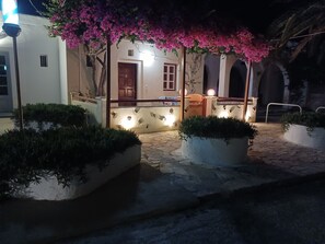 A courtyard with a stone floor, a wooden door, and a bench under a pink flowering tree. - Evelina Pension (Santorini)