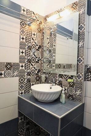 A bathroom with patterned tiles, a white sink, and a mirror. - Evelina Pension (Santorini)