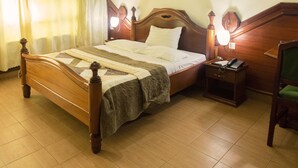 Una cama de madera con colcha, una mesita de noche con lámpara y una silla.
