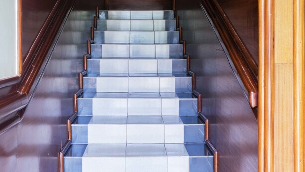 Una escalera con escalones azules y blancos alternados, barandillas de madera y techo blanco.