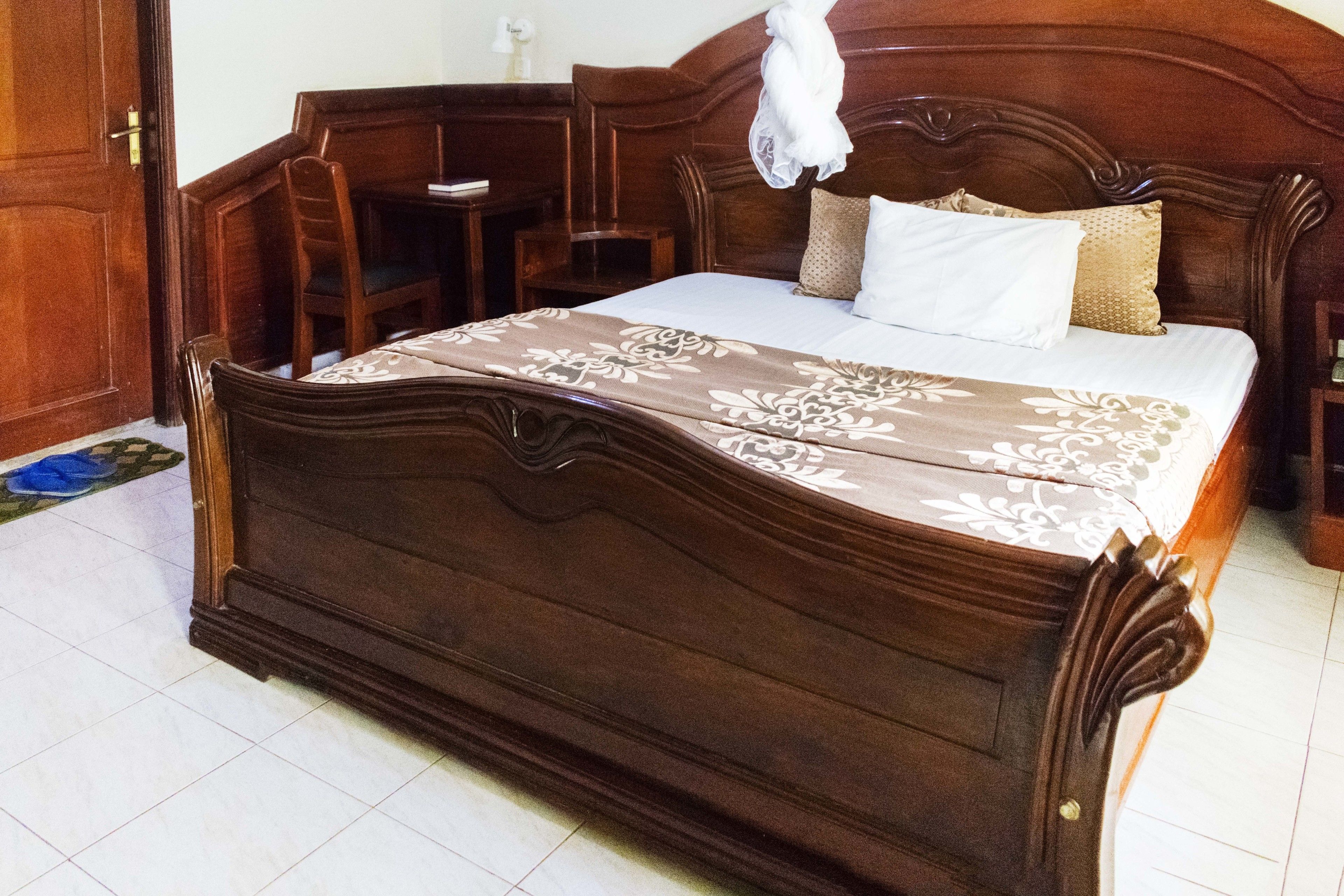 Una cama de madera con colcha floral, una mesita de noche de madera y una silla.