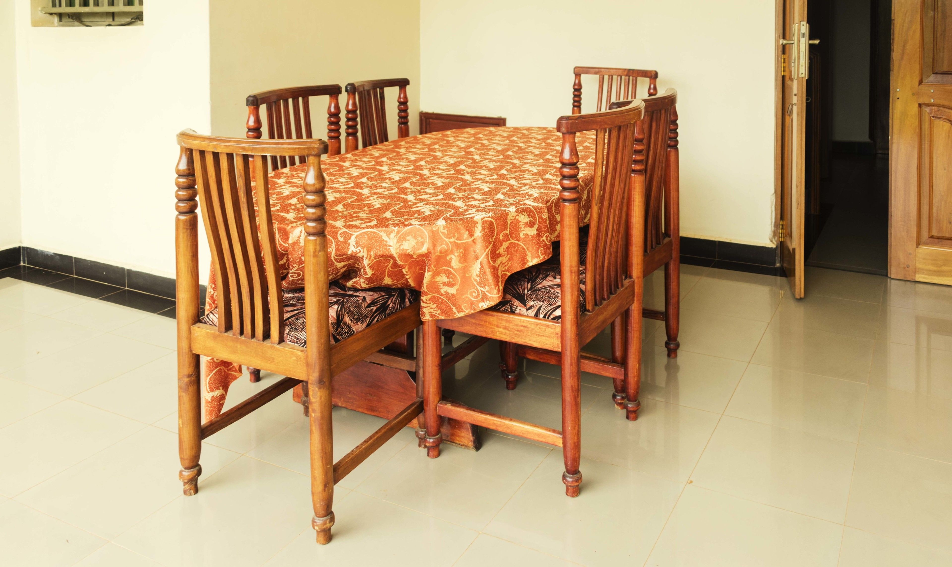 A dining table with a patterned tablecloth, surrounded by wooden chairs with cushioned seats.