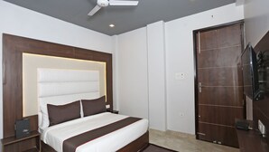 A modern hotel room with a large bed, a ceiling fan, a TV, and a wooden wardrobe. - Hotel Capital Mount (New Delhi)