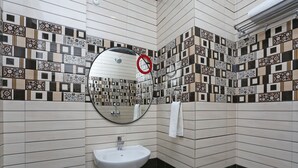 A bathroom with a white sink, a mirror, and patterned tiles on the walls. - Hotel Capital Mount (New Delhi)
