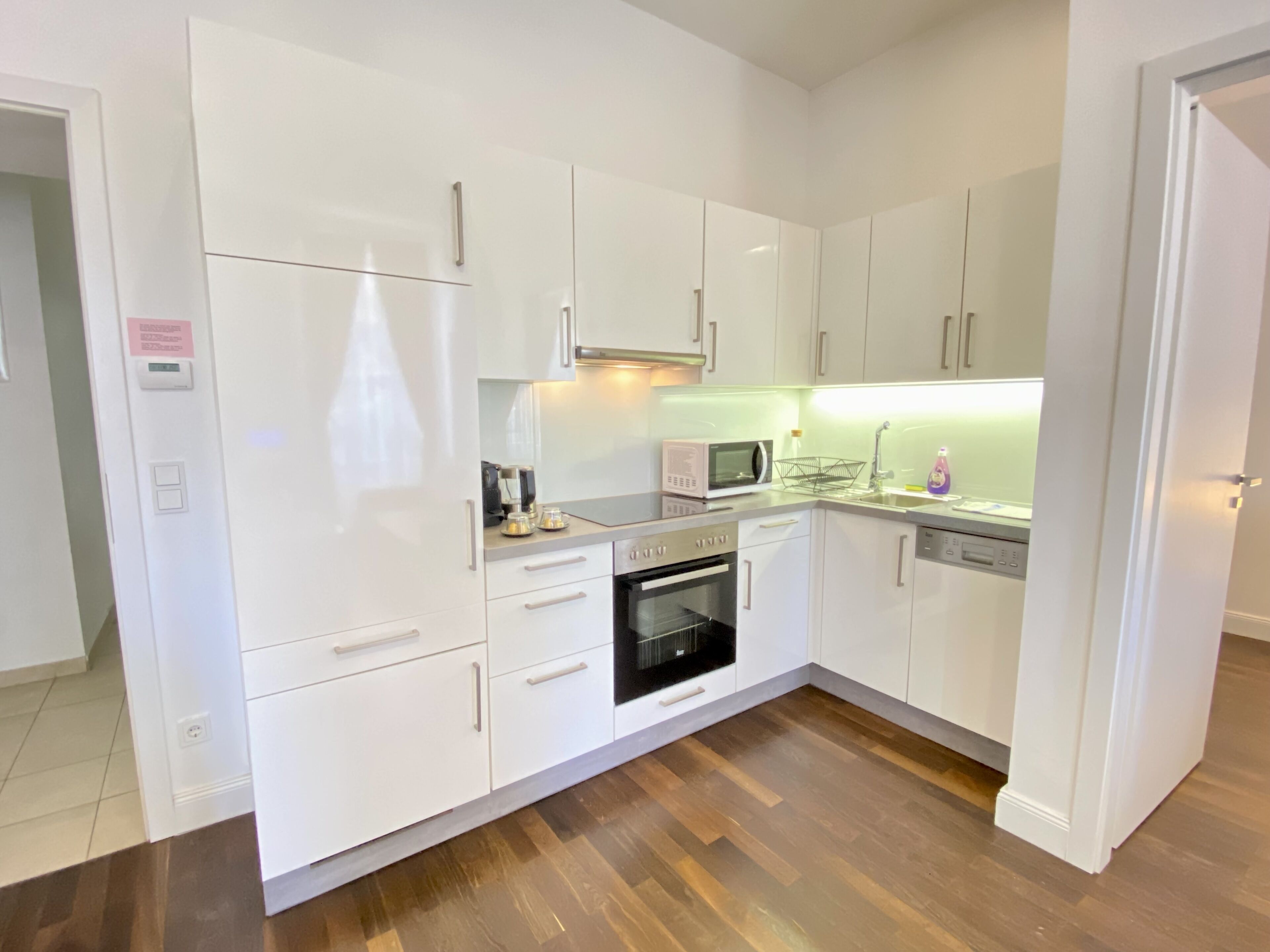 Une cuisine moderne avec des meubles blancs, un four à micro-ondes, un four traditionnel et un lave-vaisselle.