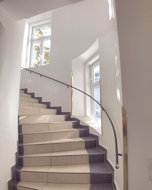 A modern staircase with a glass railing, leading to a landing with a window. - Steiner Residences Vienna Augarten (Vienna)