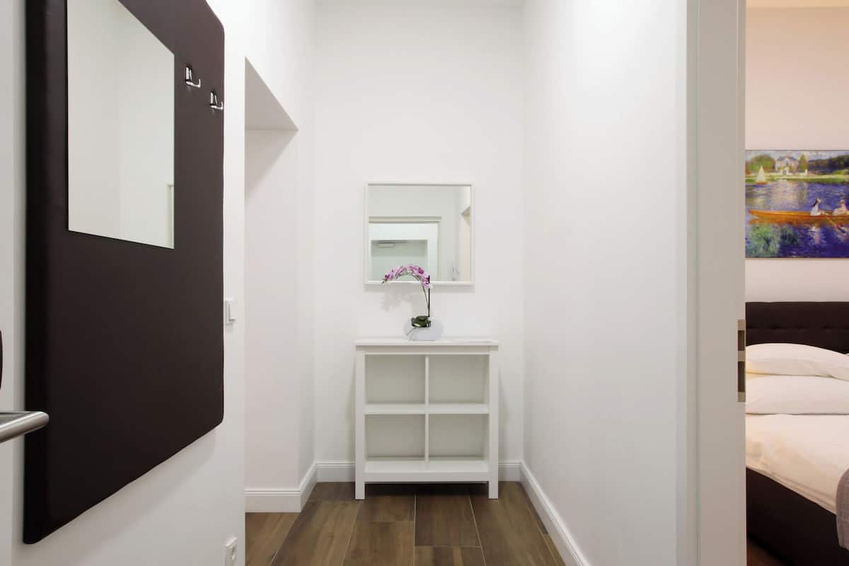 A narrow hallway with a wooden floor, a white console table with a mirror, and a door with a black frame.