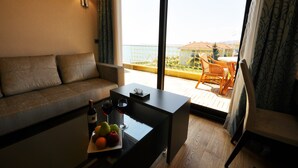 Ein Balkon mit Blick auf das Meer, eine Couch, ein Tisch mit einer Weinflasche und Obst sowie ein Stuhl.
