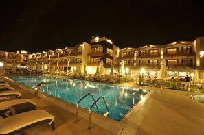 A swimming pool with lounge chairs and umbrellas, surrounded by hotel buildings with balconies and outdoor seating areas. - Venüs Termal Butik Otel (Edremit)