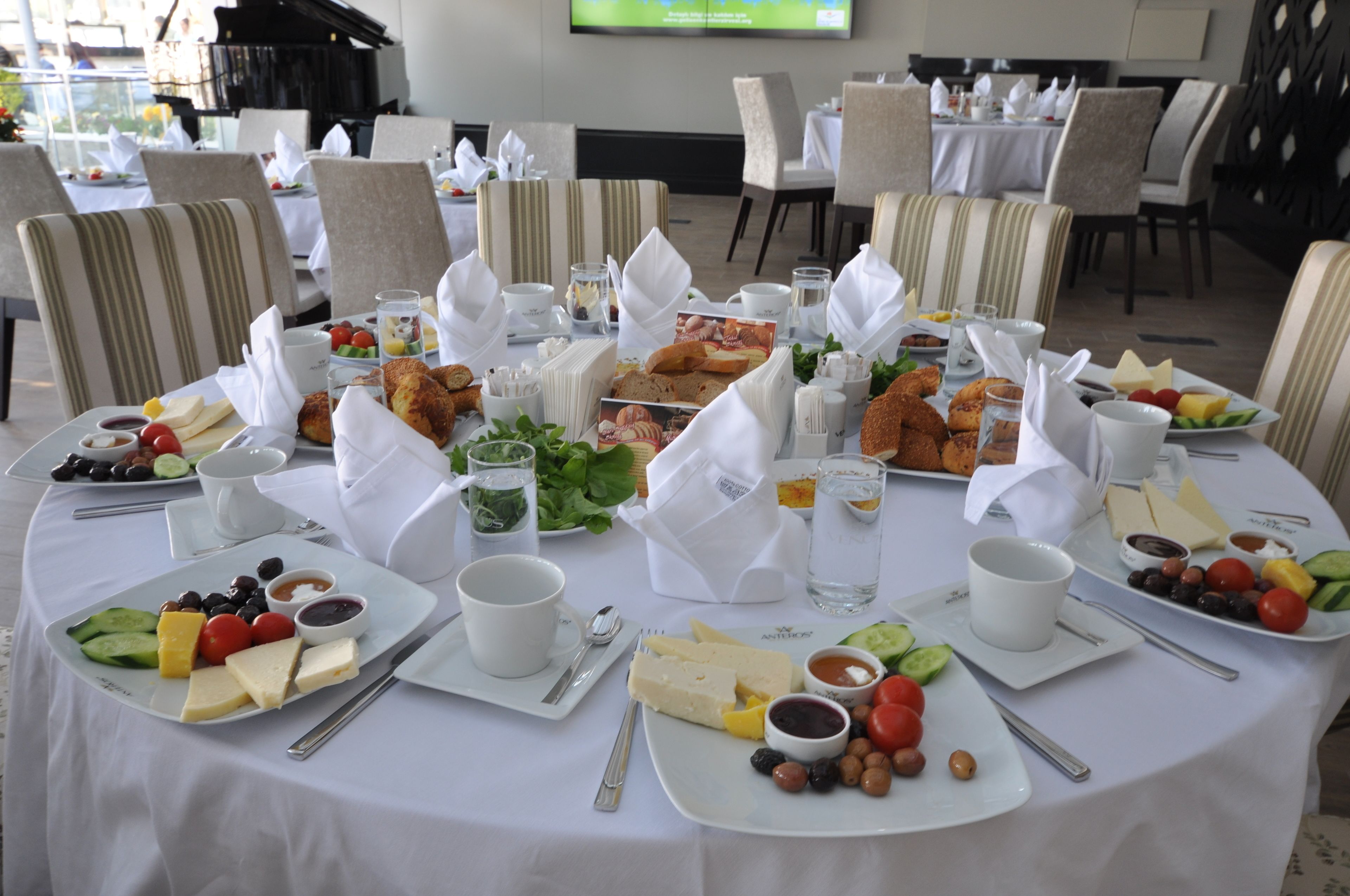 Ein Esstisch, reichhaltig gedeckt mit Käse, Obst und Brot, umgeben von Stühlen.