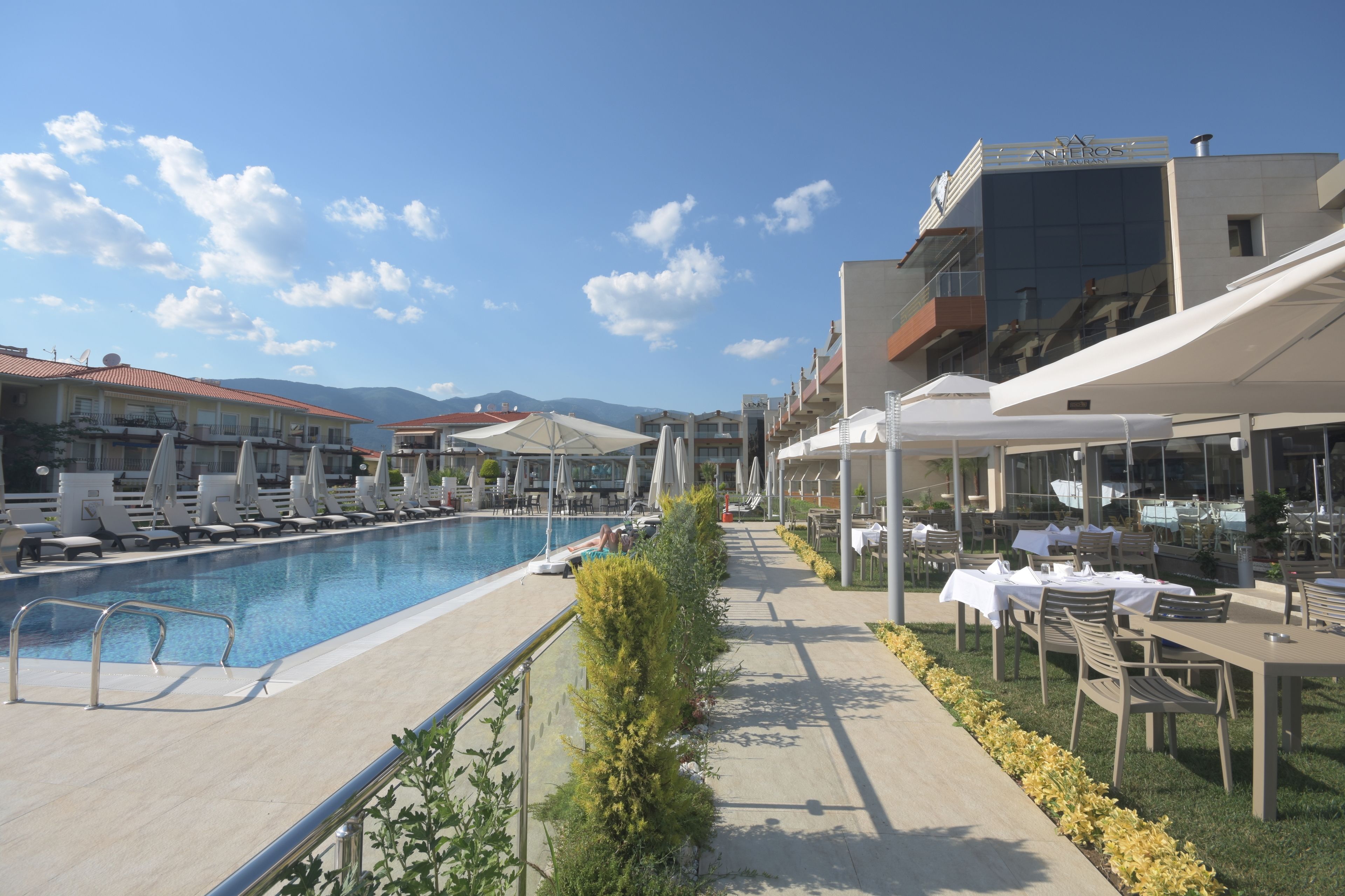 A poolside area with lounge chairs, umbrellas, and dining tables.