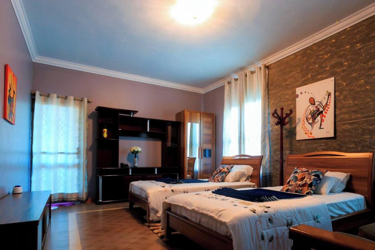 A hotel room with two beds, a wooden wardrobe, a desk, and a large window with curtains.