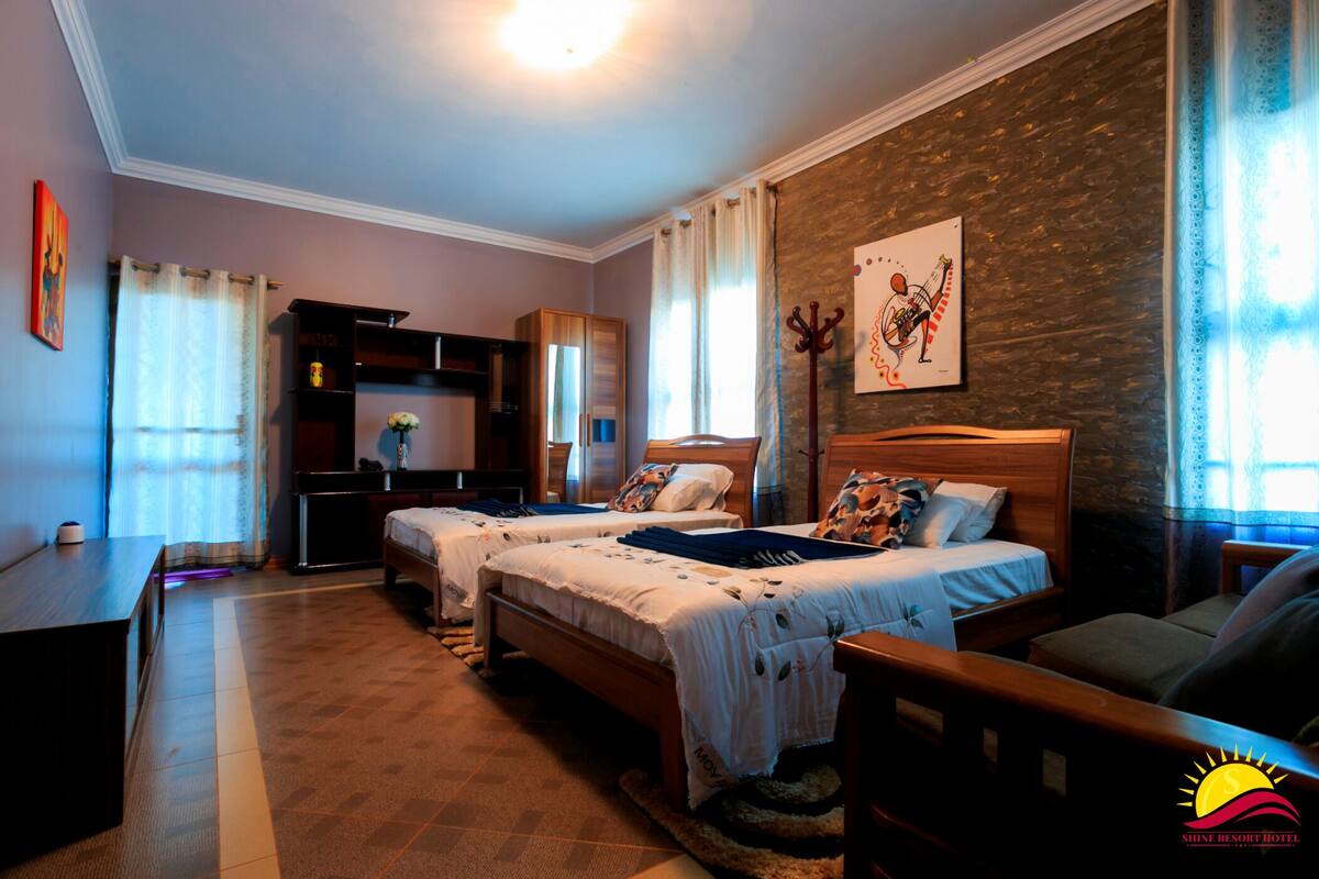 A hotel room with two beds, a desk, a wardrobe, and a large window with curtains.