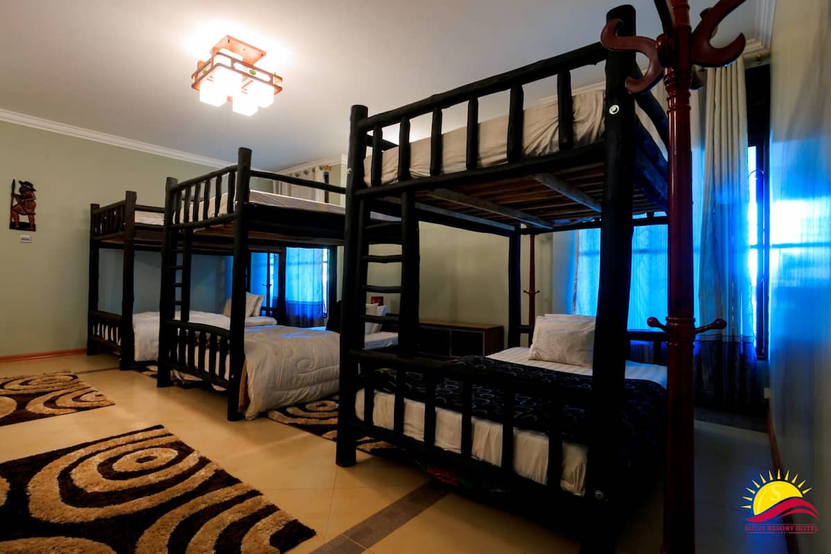 A room with three bunk beds, a wooden floor, and a patterned rug.