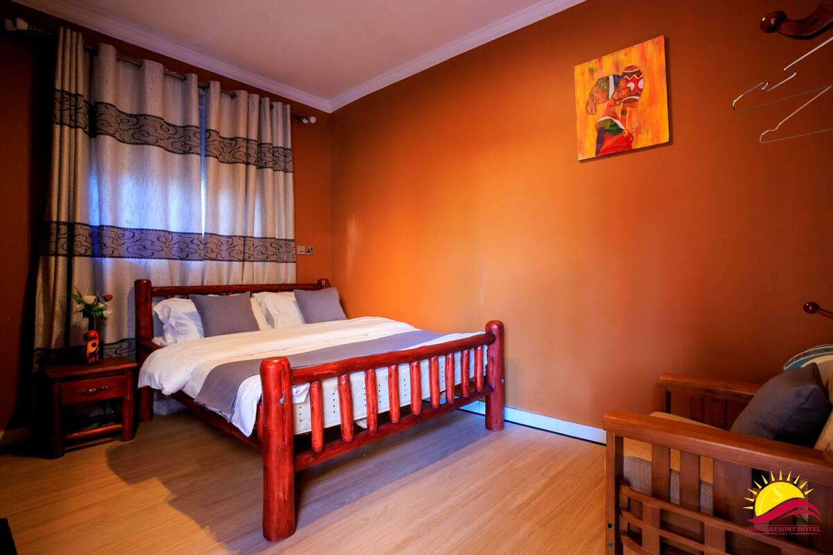 A bedroom with a wooden bed, a nightstand, a chair, a painting on the wall, and a window with curtains.