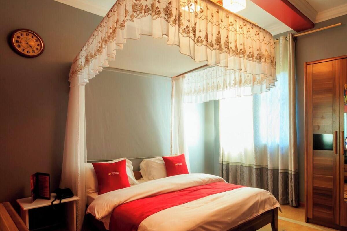 A bedroom with a four-poster bed, a bedside table with a lamp, and a wardrobe.