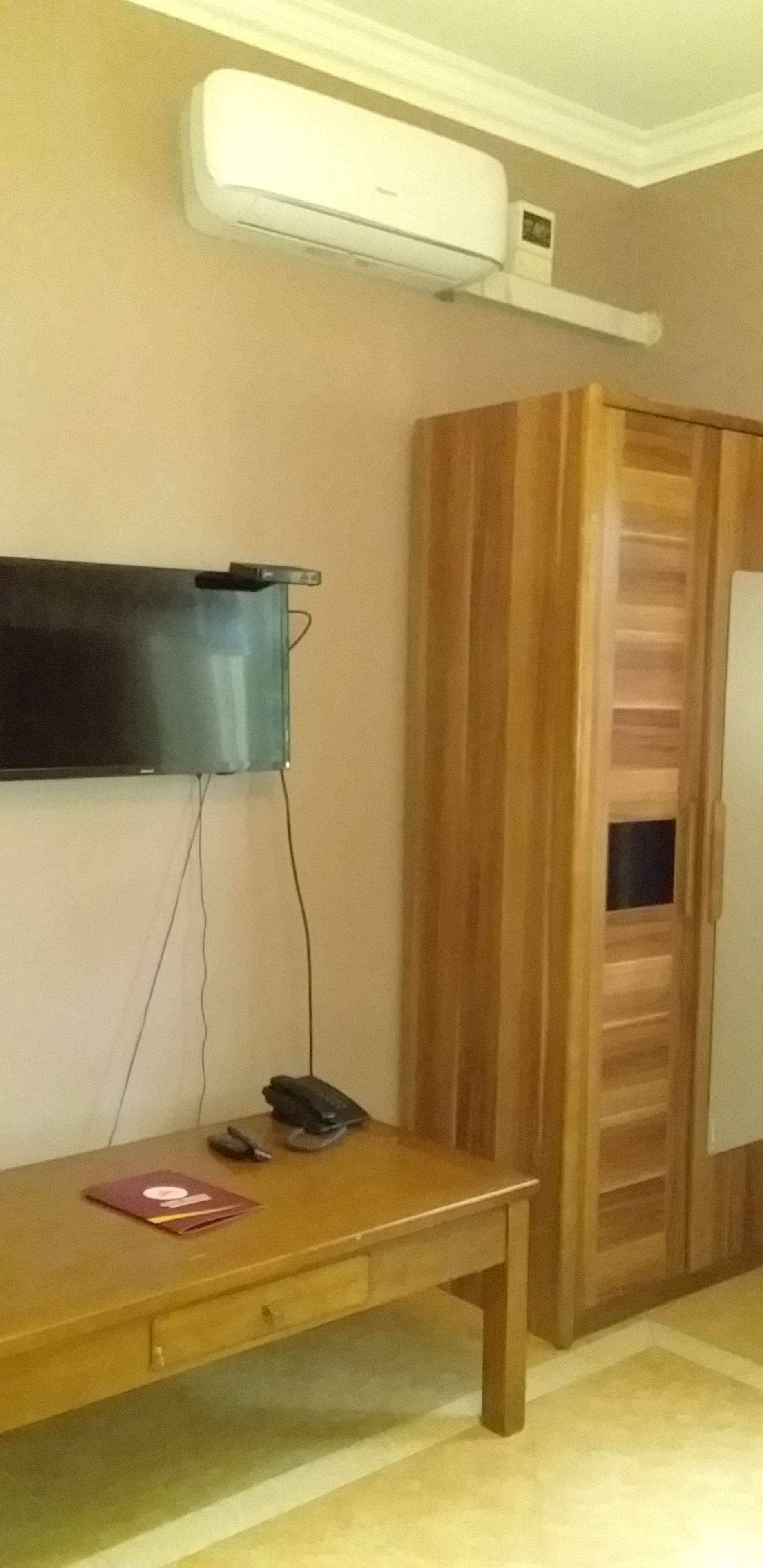A room with a wooden cabinet, a television mounted on the wall, and a desk with a computer and a phone.