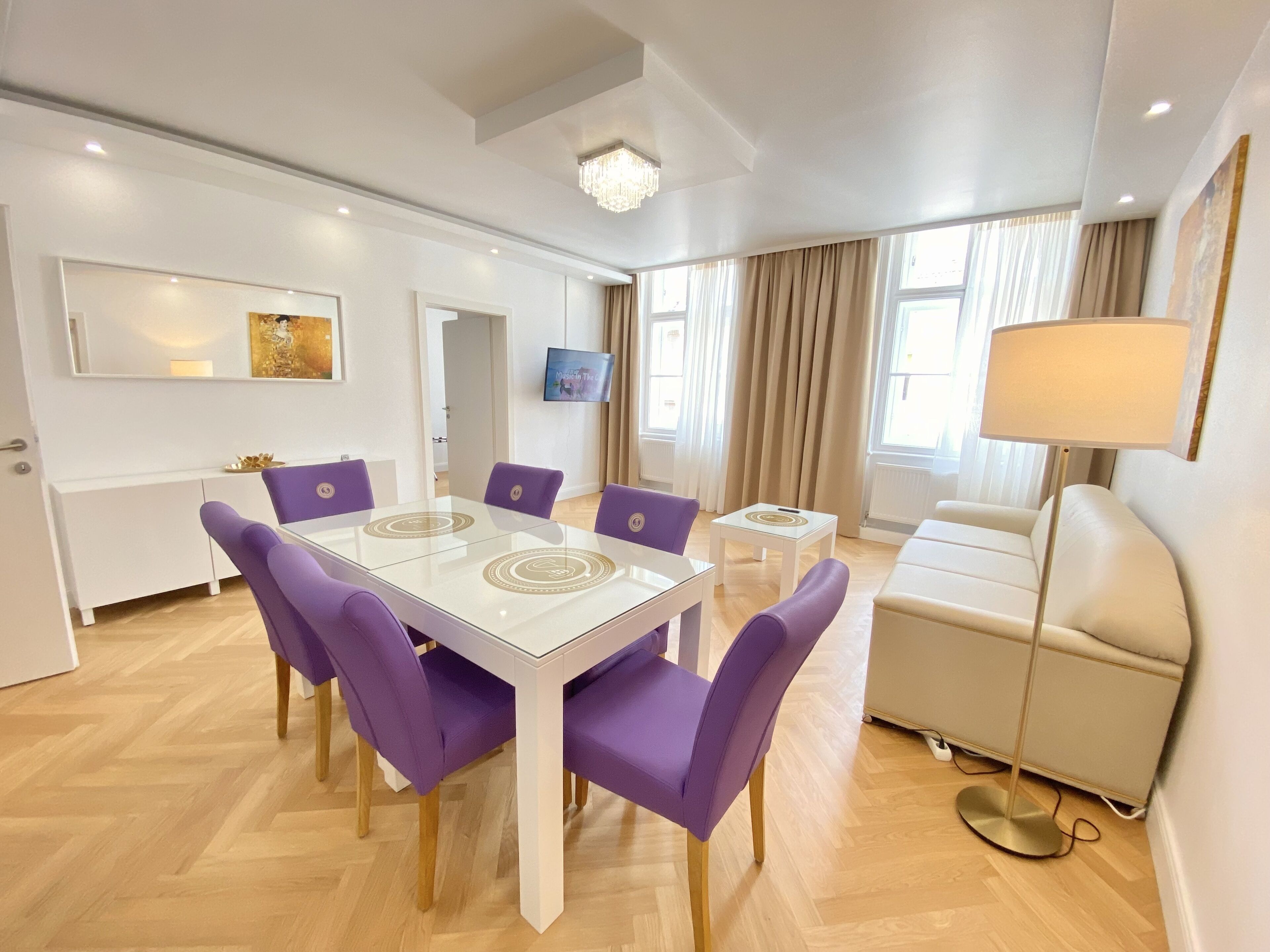 Un salon moderne avec un canapé blanc, une table basse ronde et une table à manger avec des chaises violettes.