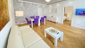 Un salon moderne avec un canapé blanc, des fauteuils violets, une table basse blanche et un mur décoré d’un motif imitant la pierre.