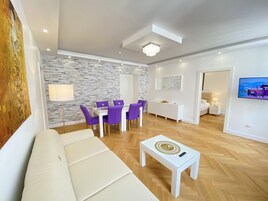 A modern living room with a white sofa, purple chairs, a white coffee table, and a stone-patterned wall.