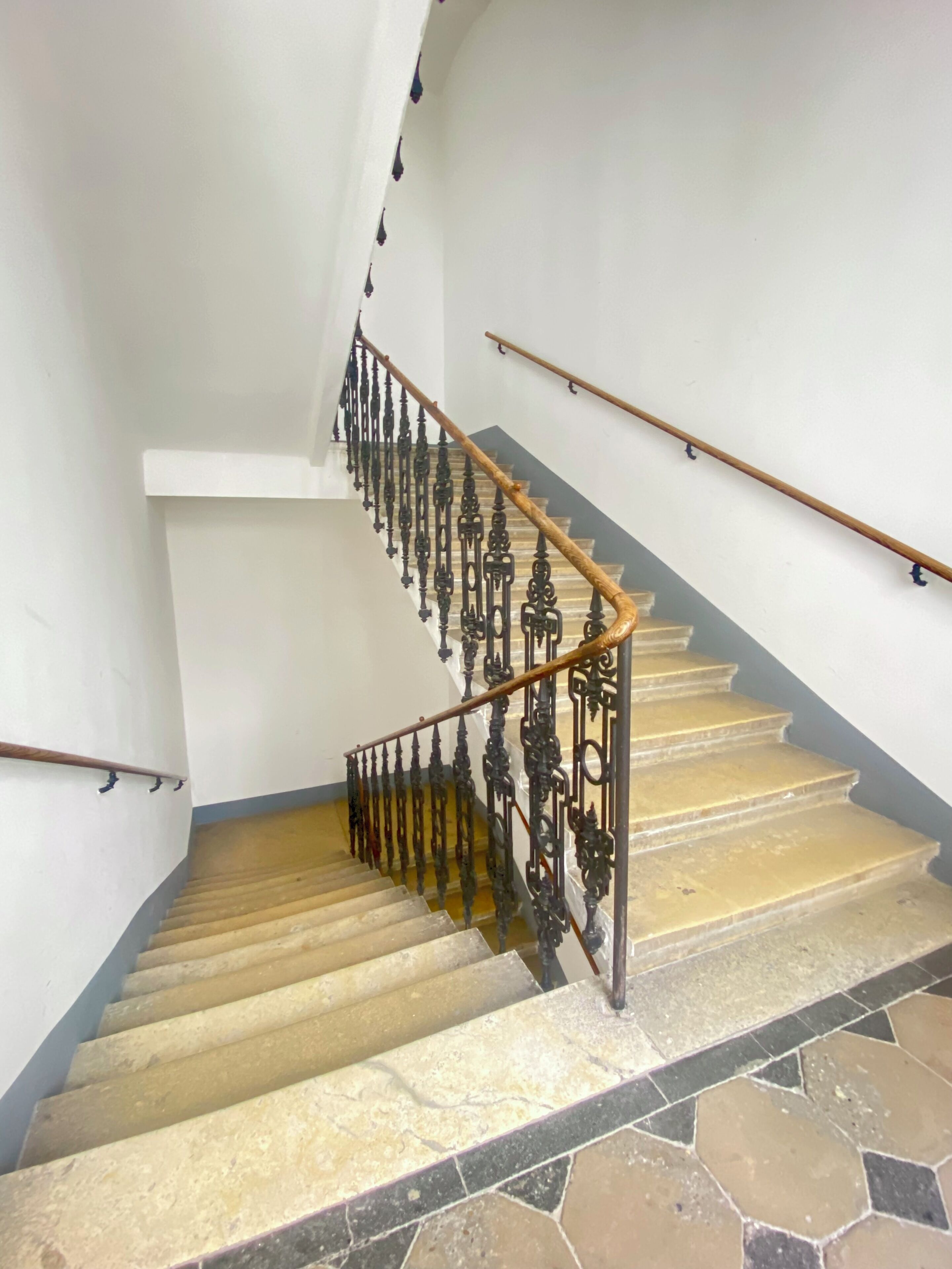 Un escalier avec une rampe, des marches en pierre et un sol carrelé.