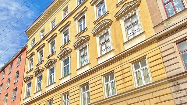Un immeuble à plusieurs étages, doté d’une façade jaune, de grandes fenêtres et d’une entrée imposante.