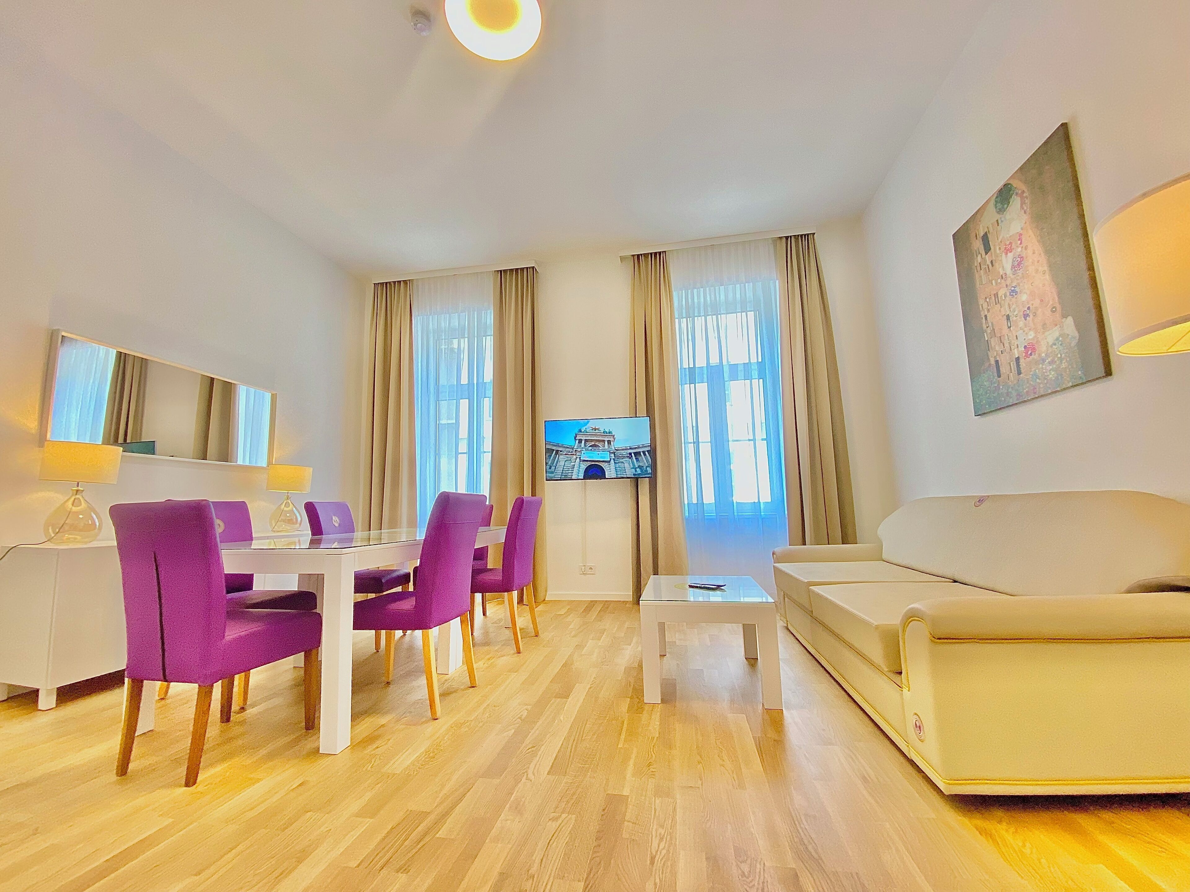 A modern living room with a dining area, a sofa, a TV, and a painting on the wall.