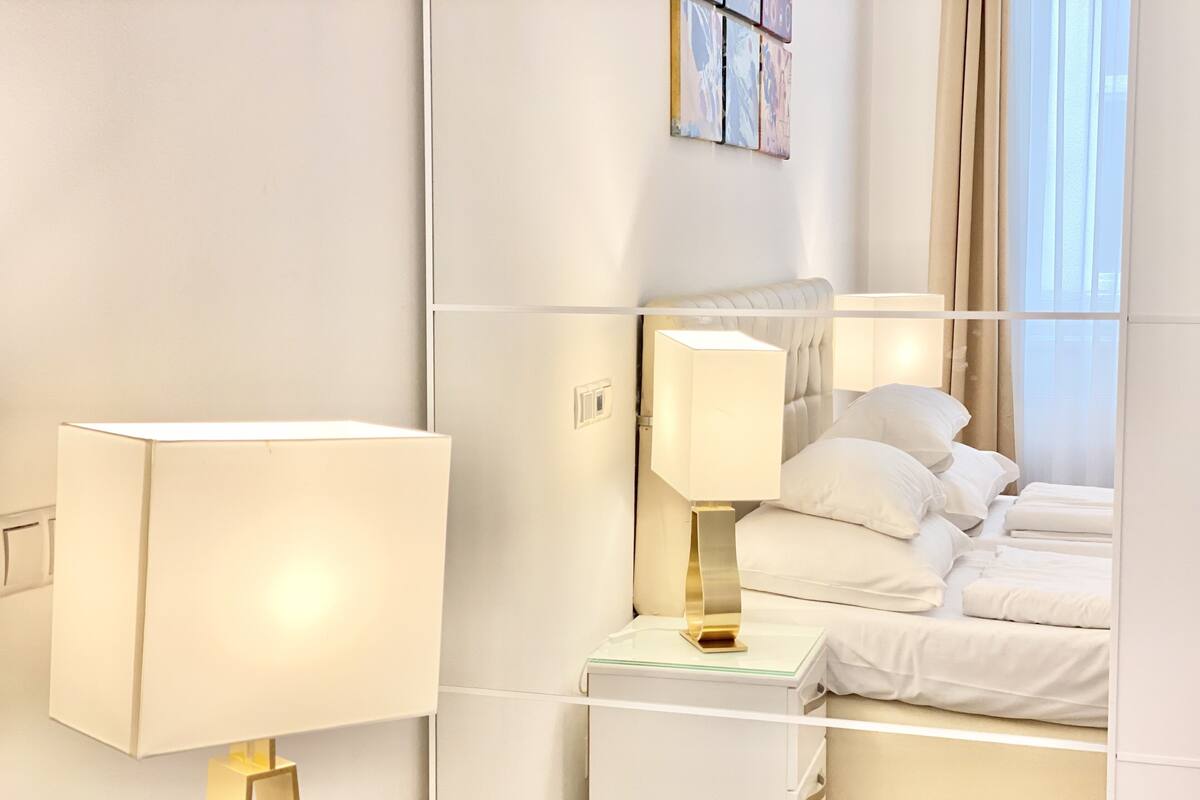 Ein Hotelzimmer mit Bett, Nachttisch, Lampe und einem Kunstwerk an der Wand.