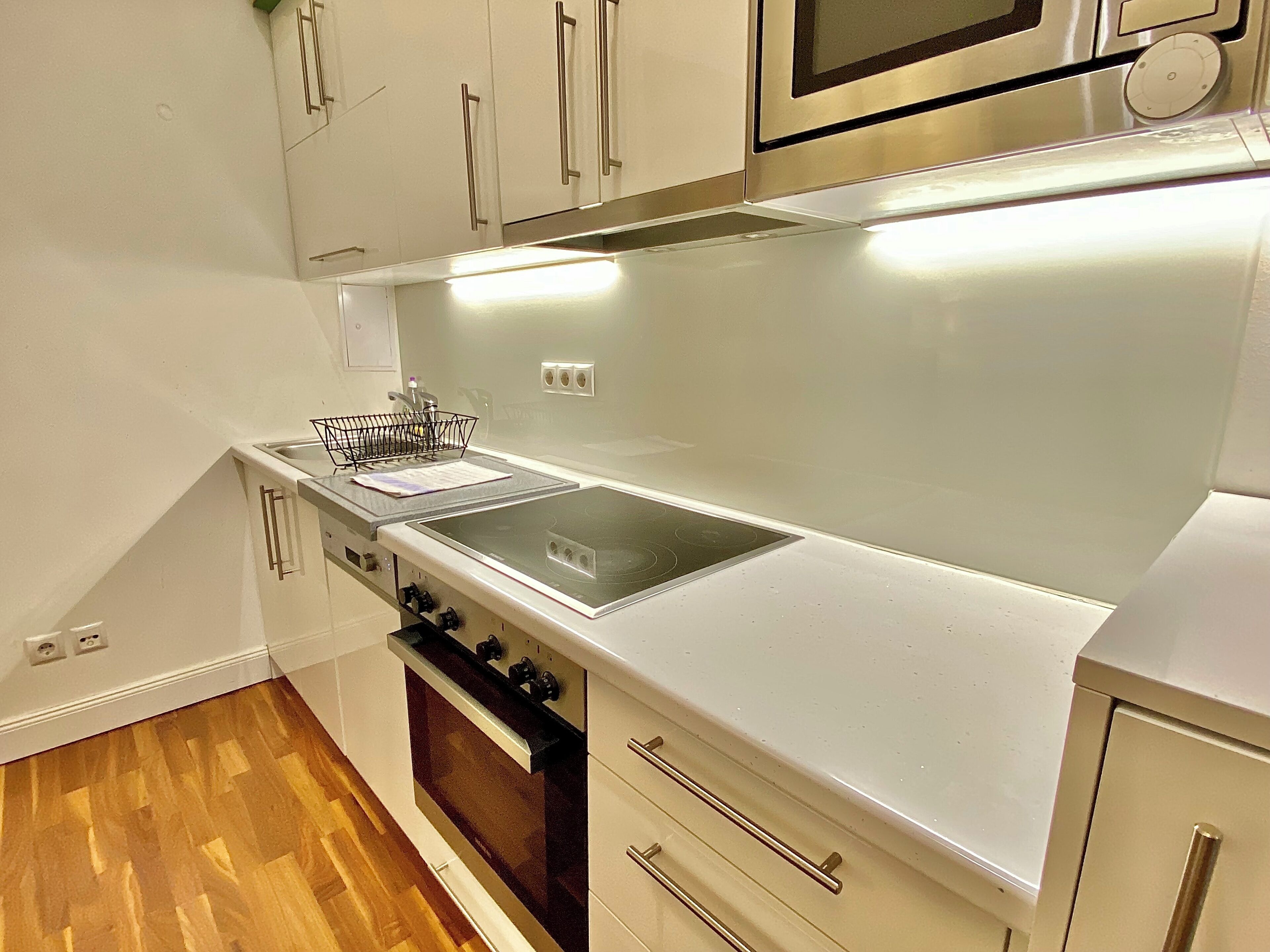 Une cuisine moderne avec des meubles blancs, une hotte en acier inoxydable, un four à micro-ondes et un plancher en bois.