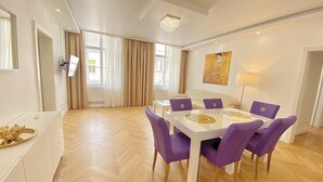 Un salon moderne avec une table à manger en verre, des chaises violettes, un canapé blanc et une grande fenêtre avec des rideaux.